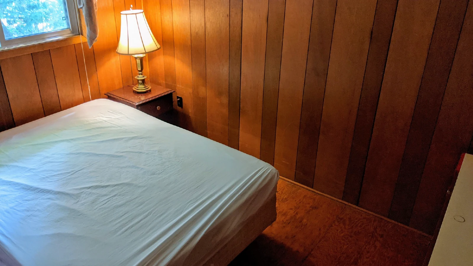 Pigeon Lake Resort Cottage nineteen, main bedroom with queen bed, wood-paneled walls, bedside table, and lamp by window.